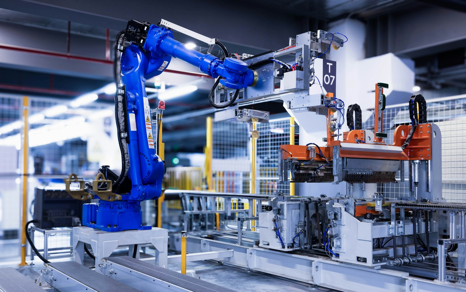 A blue industrial robot arm working on an automated production line, station T07, behind safety fencing
